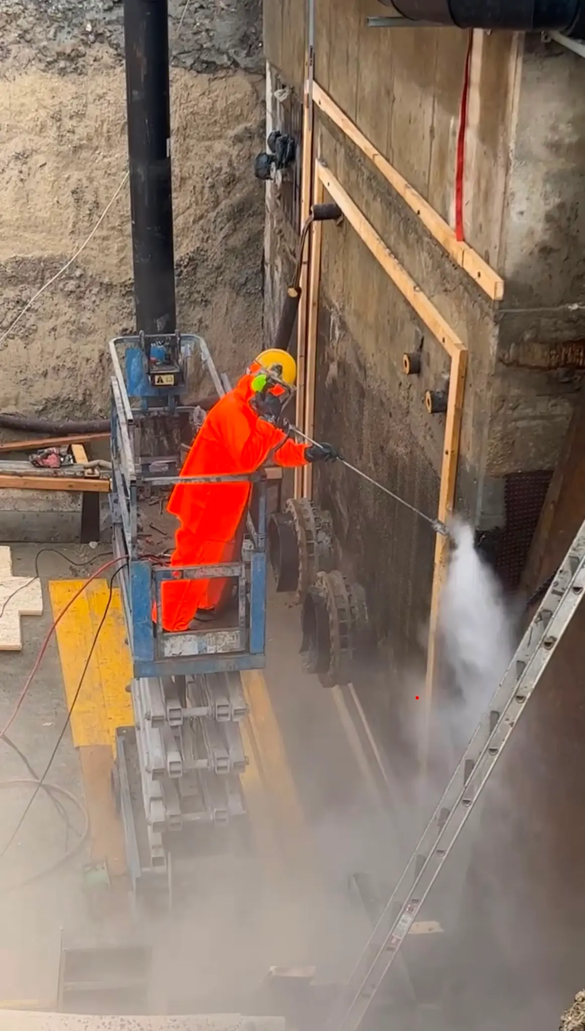 Operatør i orange dragt arbejder fra en lift med UHP-lanse mod en betonvæg, mens vandet står som en sky under strålen.